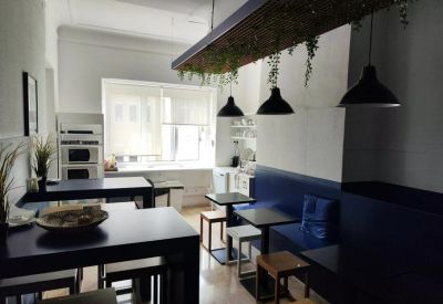 Bright communal kitchen and dining area with blue bench seating and hanging plants.
