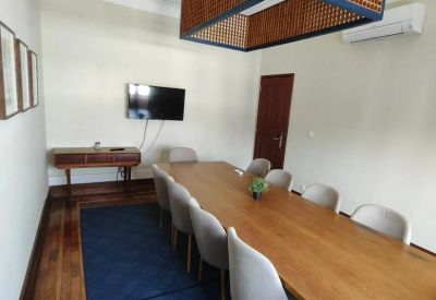 Spacious boardroom with a long wooden table, blue rug, and a large decorative light fixture.