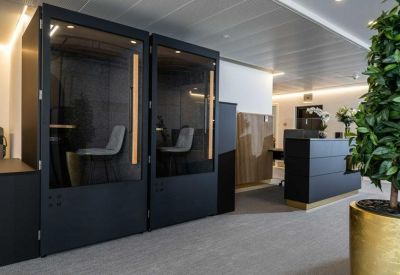 Reception area with a dark sleek desk, modern private phone booths, and indoor greenery.