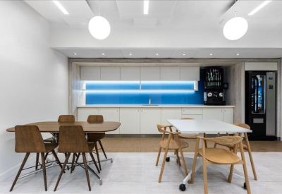 Communal break area with wooden tables, a kitchen, and a blue neon backsplash.