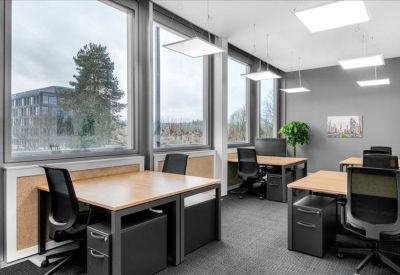 Bright open-plan office with multiple desks, black chairs, and large windows.