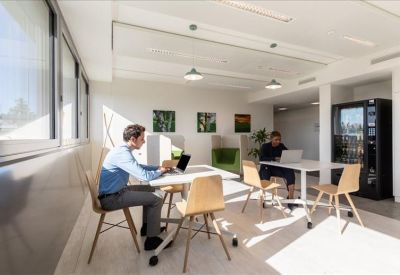 Coworking space with wooden chairs and people working at white tables.
