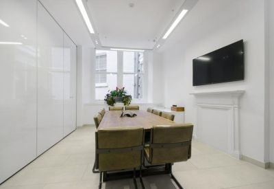 Sleek meeting room with a large wooden table, tan chairs, and a minimalist white feature wall.