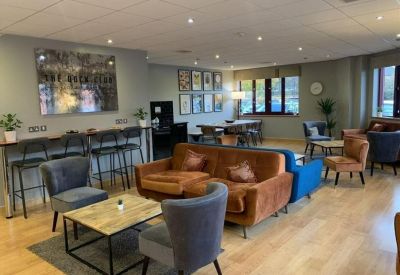 Bright breakout lounge with colorful sofas, bar seating, and wooden flooring.