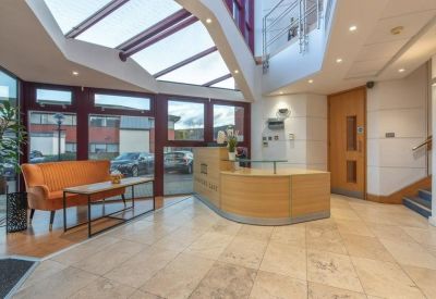 Modern reception lobby with a curved wooden desk and bright atrium ceiling.
