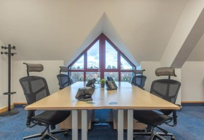 Modern office space with desks and ergonomic chairs positioned under a gabled window.