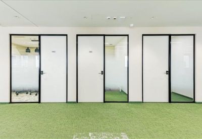 Row of private office suites with white doors and glass sidelights on green carpeting.