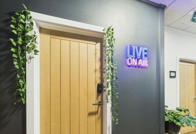 Wooden door entrance with a Live On Air neon sign and decorative vines.