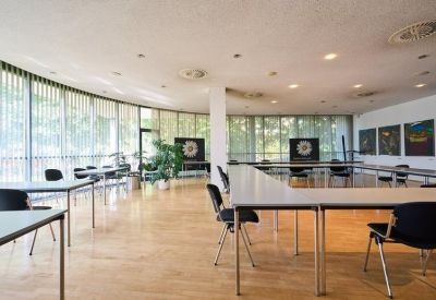 Bright, curved communal lounge and meeting area with wooden floors, indoor plants, and large windows.