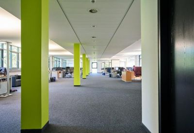 Spacious open-plan office corridor featuring vibrant lime green structural pillars and grey carpeting.