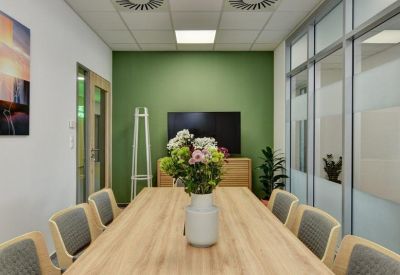 Small meeting room with a wooden table, grey chairs, and a green feature wall.