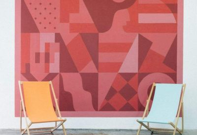Lounge area featuring two canvas deck chairs in front of a large geometric mural in red tones.