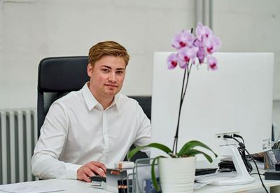 Bright office desk with a large computer monitor and a purple orchid plant.