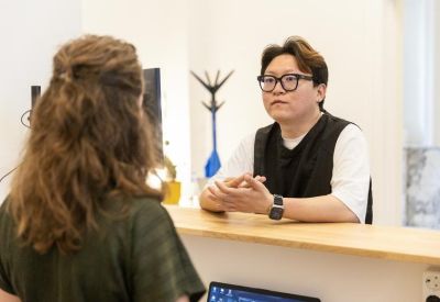 Bright reception desk with a staff member wearing glasses talking to a visitor.