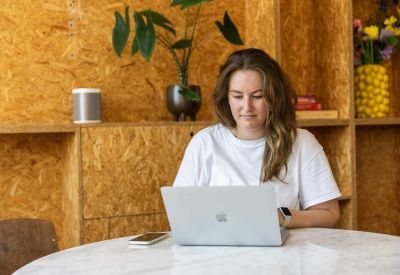 A woman working on a laptop at a marble table against a textured light wood wall.