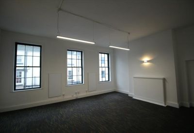 Spacious, white-walled private office with dark carpeting and three large sash windows.