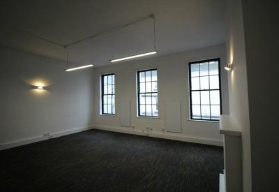 Bright, empty office space featuring suspended linear lighting and natural light from large windows.