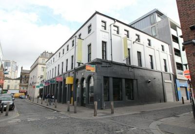 Street-level view of the white and dark grey building exterior with multiple arched windows.