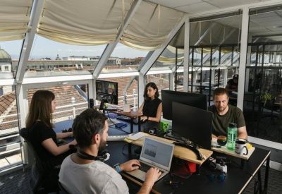 Sunlit coworking space with people working at desks under a sloped glass roof.