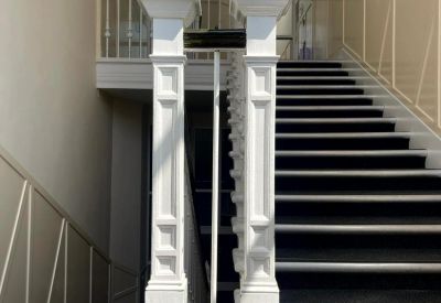 Grand internal staircase with ornate white banister posts and black carpeted steps.