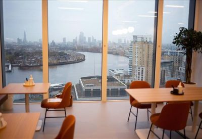 Communal dining and breakout area with wooden tables and leather chairs by a large window.