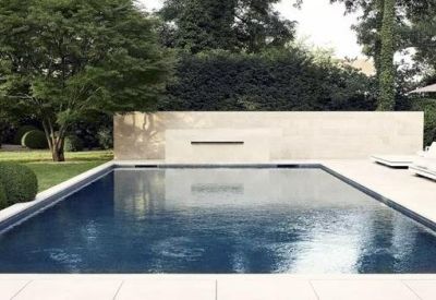 Outdoor swimming pool area with a sleek stone wall and garden seating.