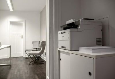 Office corridor showing a printer station and comfortable grey waiting chairs.