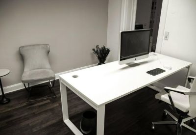 Private office suite with a white desk, large monitor, and dark wood flooring.