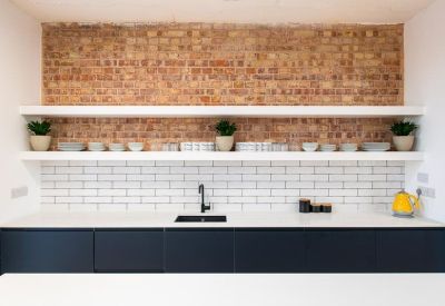 Modern kitchen with black cabinetry, white countertops, and an exposed brick feature wall.