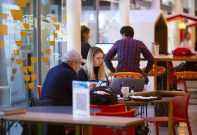 Casual coworking lounge with people working at wooden tables and red chairs.