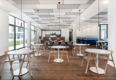 Bright communal lounge and cafe area with round tables and wooden floors.