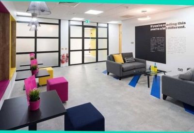 Bright communal lounge with colorful stools, grey sofas, and glass partition walls.