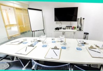 Professional meeting room featuring a white boardroom table and wall-mounted screen.