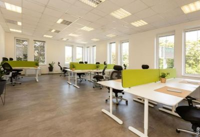 Spacious open-plan workspace with multiple ergonomic desks, green privacy screens, and natural light.