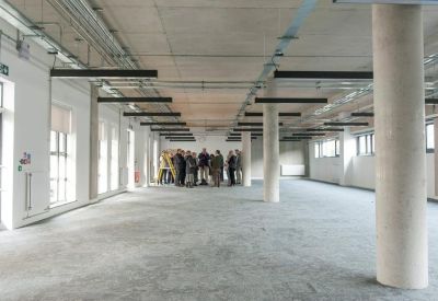 Spacious open-plan office shell with industrial concrete pillars and exposed ceiling tracks.