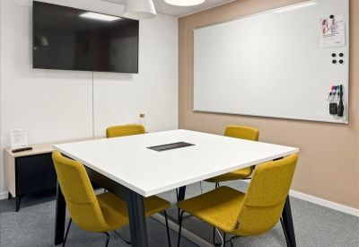 Modern meeting room with a white square table, yellow chairs, and a wall-mounted TV.