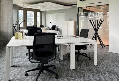 Open-plan office space with multiple white desks and ergonomic black chairs.
