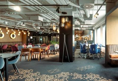 Spacious coworking cafe area with diverse seating and exposed ceiling pipes.