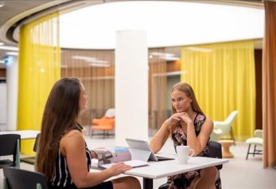 Long white conference table with grey chairs and modern pendant lighting against a gallery wall.