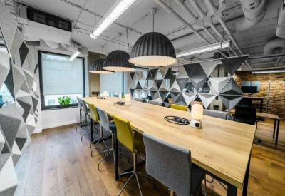 Long wooden coworking table with colorful chairs under large dome pendant lights and geometric wall art.