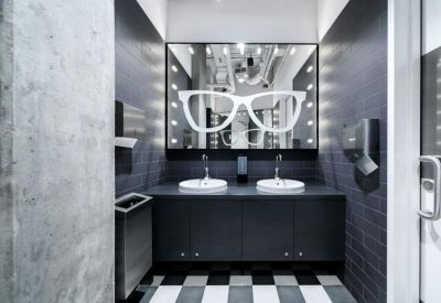 Modern restroom with dark cabinetry, dual sinks, and a large mirror featuring a neon glasses graphic.