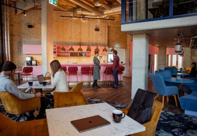 Lounge area with a pink counter, blue armchairs, and people working at tables.