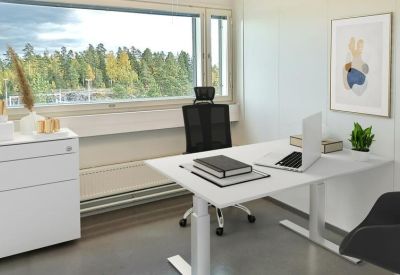 Private office with an adjustable sit-stand desk, black ergonomic chair, and a large window overlooking trees.