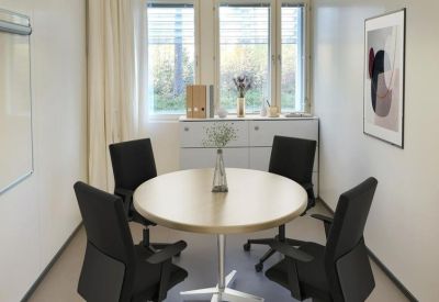 Small meeting room with a round wooden table, four black chairs, and a whiteboard.
