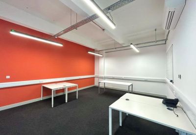 Spacious office with a bright orange feature wall and three white workstations.