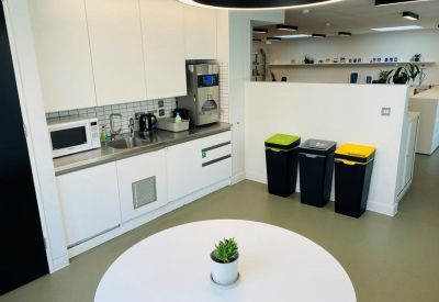 Modern kitchenette with white cabinets, built-in appliances, and colorful recycling bins.