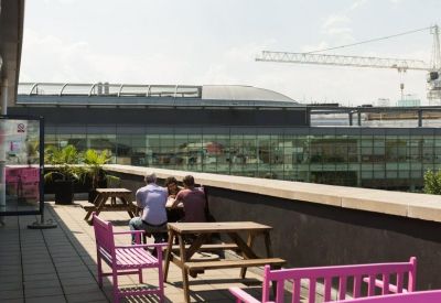 Sunny rooftop terrace with picnic tables and a distant city skyline view.