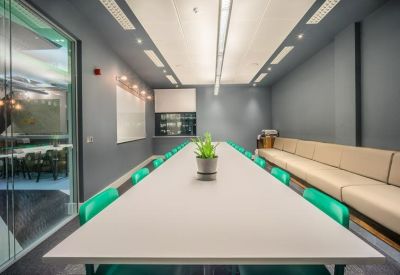 Long white boardroom table in a sleek grey meeting room with teal chairs.