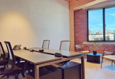 Private office suite with a four-person desk and a casual seating area by a brick feature wall.