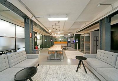 Spacious communal lounge with grey sofas, a long wooden table, and industrial metal beams.